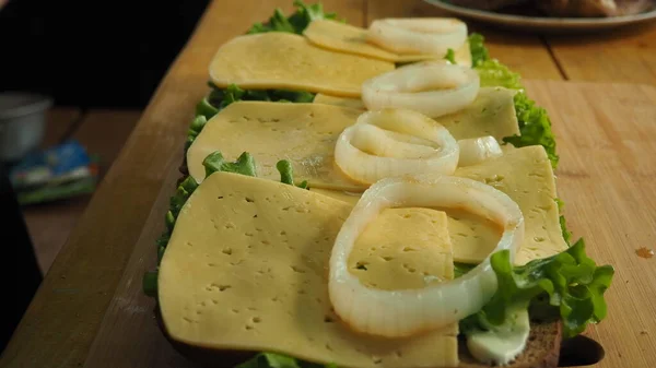 厨师在面包上放生菜叶和带有洋葱圈的奶酪 — 图库照片