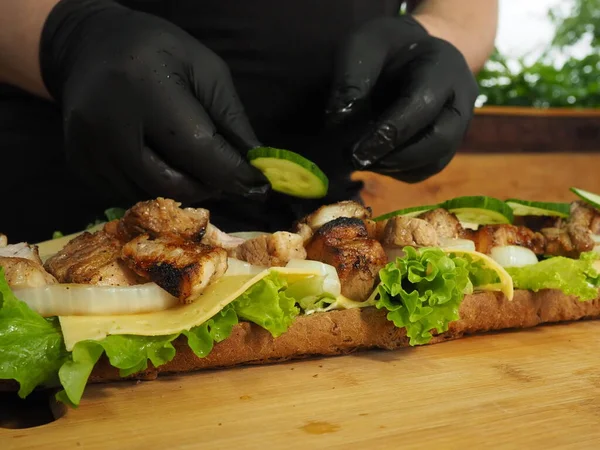 Şef, Fransız ekmeğinden bir sandviç hazırlıyor. Yeşillik, peynir ve etle birlikte. sandviç