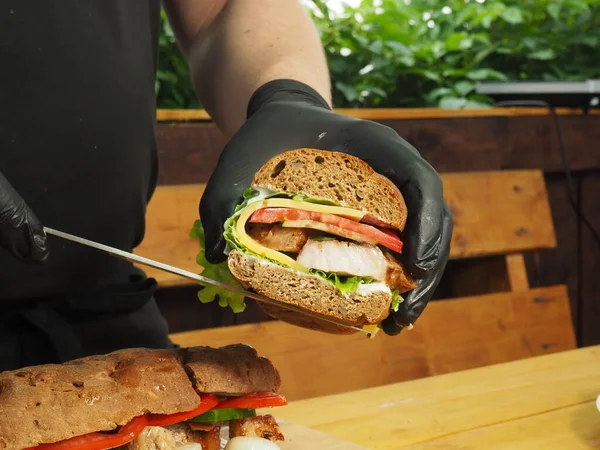 Bir şef yeşil, peynirli ve etli Fransız baget sandviçi gösterir.