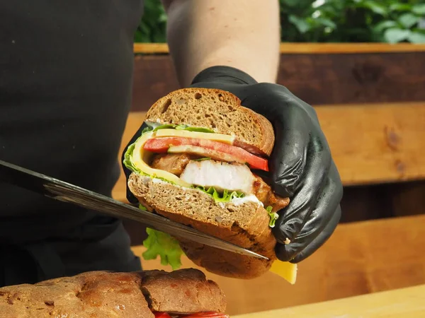 Bir şef yeşil, peynirli ve etli Fransız baget sandviçi gösterir.