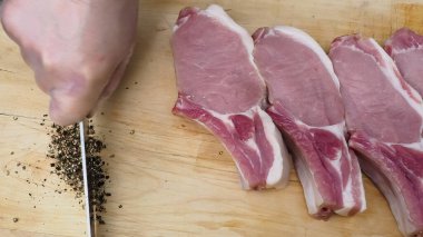 Aşçı domuz bifteğine biber ve tuz serpiyor. Et pişirmek. Salamura edilmiş domuz eti.
