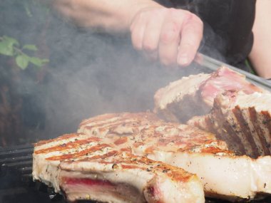Aşçı domuz bifteğini ızgaradaki kemiklere çevirir. Izgara için maşa.