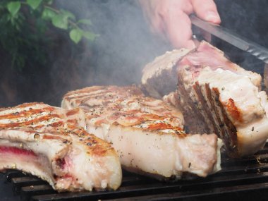 Aşçı domuz bifteğini ızgaradaki kemiklere çevirir. Izgara için maşa.