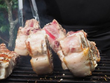 Siyah önlüklü bir aşçı kemiklerinde biftek pişirir. Kemikte ızgara domuz eti. Izgara için maşa.