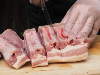 Eldivenli ve siyah önlüklü bir şef domuz filetosunu biftek şeklinde keser. Biftek pişirmek. Et. Domuz. Yemek pişirme posteri.