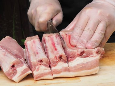 Eldivenli ve siyah önlüklü bir şef domuz filetosunu biftek şeklinde keser. Biftek pişirmek. Et. Domuz. Yemek pişirme posteri.