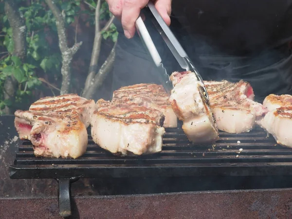 the cook turns the pork steaks on the bones on the grill. tongs for grilling.