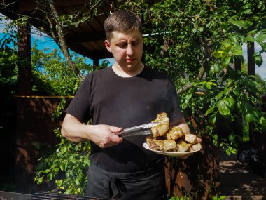 Genç bir adam ızgara ızgarasından maşayla biftek çıkartıyor. Aşçı. Domuz bifteği.