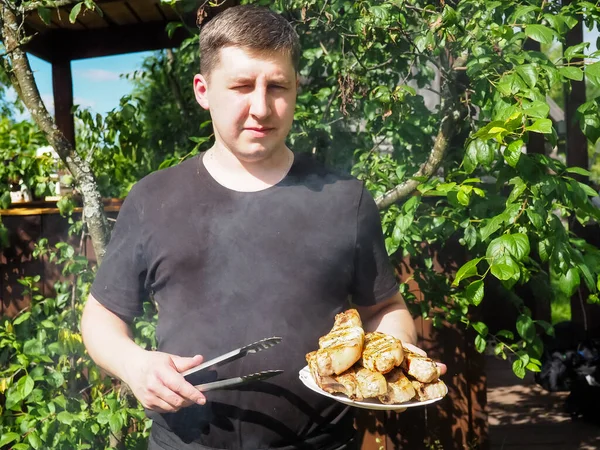 Genç bir adam ızgara ızgarasından maşayla biftek çıkartıyor. Aşçı. Domuz bifteği.