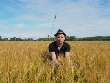 Şapkalı bir adam arpa tarlasında oturur. Hasat. çiftlik alanı.