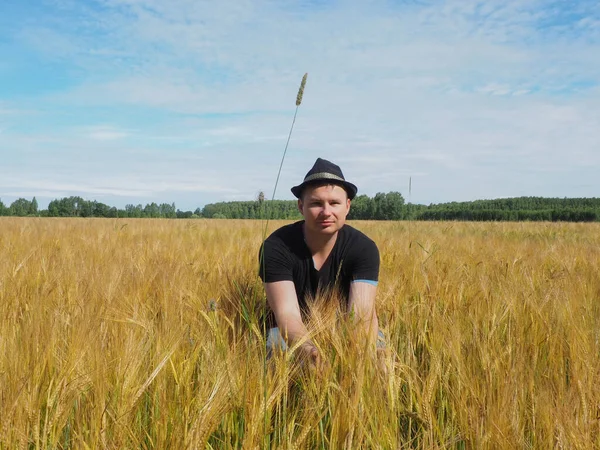 Şapkalı bir adam arpa tarlasında oturur. Hasat. çiftlik alanı.