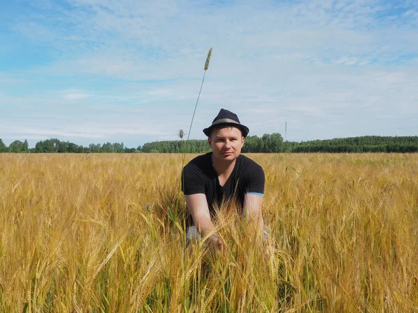 Şapkalı bir adam arpa tarlasında oturur. Hasat. çiftlik alanı.