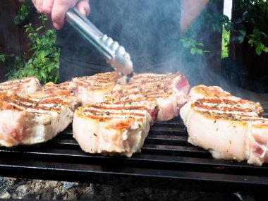 Adam biftekleri maşayla çeviriyor. Kömürde pişirmek. Kemiklerdeki domuz eti.