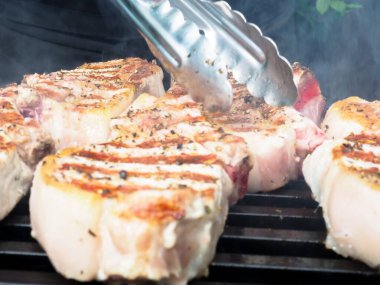 Adam biftekleri maşayla çeviriyor. Kömürde pişirmek. Kemiklerdeki domuz eti.