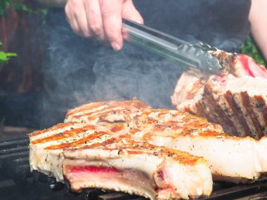 Adam biftekleri maşayla çeviriyor. Kömürde pişirmek. Kemiklerdeki domuz eti.