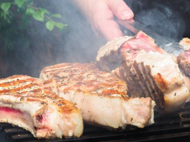 Adam biftekleri maşayla çeviriyor. Kömürde pişirmek. Kemiklerdeki domuz eti.