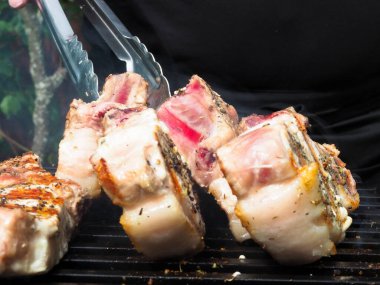 Adam biftekleri maşayla çeviriyor. Kömürde pişirmek. Kemiklerdeki domuz eti.