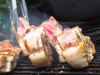 Adam biftekleri maşayla çeviriyor. Kömürde pişirmek. Kemiklerdeki domuz eti.