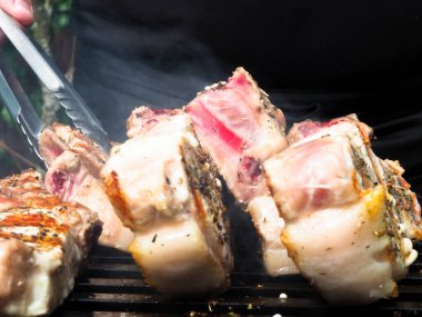 Adam biftekleri maşayla çeviriyor. Kömürde pişirmek. Kemiklerdeki domuz eti.