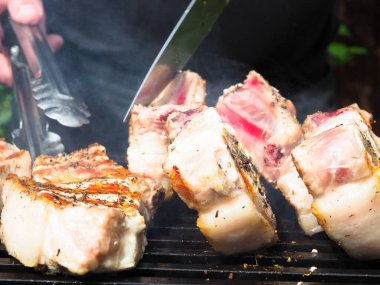 Adam biftekleri maşayla çeviriyor. Kömürde pişirmek. Kemiklerdeki domuz eti.