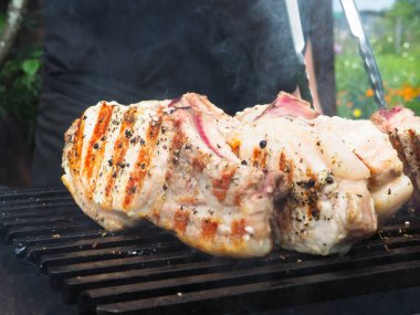 Adam biftekleri maşayla çeviriyor. Kömürde pişirmek. Kemiklerdeki domuz eti.