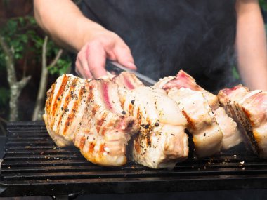Adam biftekleri maşayla çeviriyor. Kömürde pişirmek. Kemiklerdeki domuz eti.