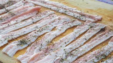 Baharatlı bir panoda dilimlenmiş çiğ domuz pastırması. Biber yağı ve bitkilerle. Lezzetli yemek.