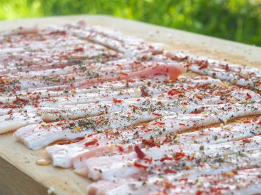 Baharatlı bir panoda dilimlenmiş çiğ domuz pastırması. Biber yağı ve bitkilerle. Lezzetli yemek.