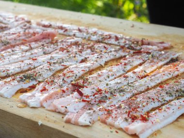 Baharatlı bir panoda dilimlenmiş çiğ domuz pastırması. Biber yağı ve bitkilerle. Lezzetli yemek.