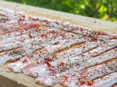 Baharatlı bir panoda dilimlenmiş çiğ domuz pastırması. Biber yağı ve bitkilerle. Lezzetli yemek.