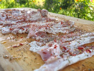 Baharatlı bir panoda dilimlenmiş çiğ domuz pastırması. Biber yağı ve bitkilerle. Lezzetli yemek.