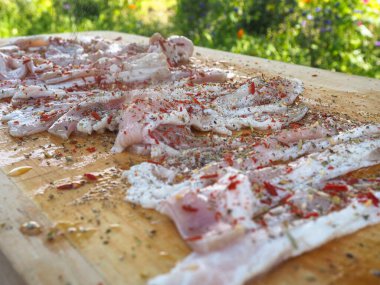 Baharatlı bir panoda dilimlenmiş çiğ domuz pastırması. Biber yağı ve bitkilerle. Lezzetli yemek.