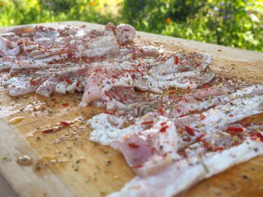 Baharatlı bir panoda dilimlenmiş çiğ domuz pastırması. Biber yağı ve bitkilerle. Lezzetli yemek.