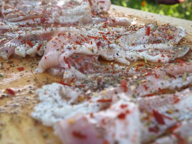 Baharatlı bir panoda dilimlenmiş çiğ domuz pastırması. Biber yağı ve bitkilerle. Lezzetli yemek.