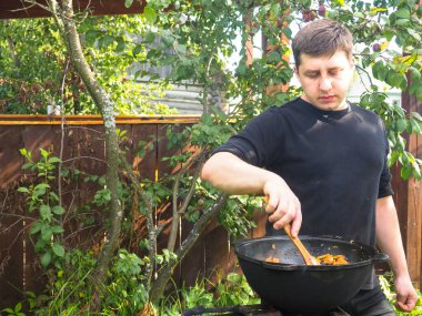 Genç adam ateşte bir kazanda yemek pişiriyor. Kazanda et pişirmek.
