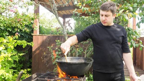 Genç adam ateşte bir kazanda yemek pişiriyor. Kazanda et pişirmek.