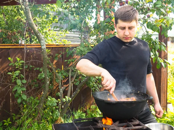 Genç adam ateşte bir kazanda yemek pişiriyor. Kazanda et pişirmek.