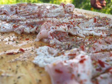 Baharatlı bir panoda dilimlenmiş çiğ domuz pastırması. Biber yağı ve bitkilerle. Lezzetli yemek.