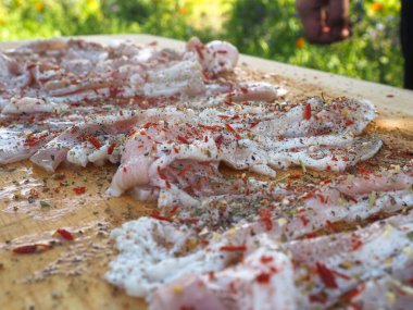 Baharatlı bir panoda dilimlenmiş çiğ domuz pastırması. Biber yağı ve bitkilerle. Lezzetli yemek.