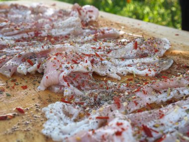 Baharatlı bir panoda dilimlenmiş çiğ domuz pastırması. Biber yağı ve bitkilerle. Lezzetli yemek.