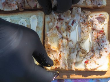 Pastırmalı sandviç yapıyorum. Eldivenli eller sandviçleri toplar.