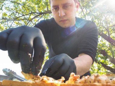 Siyah eldivenli yemek hazırlamak için doğadaki adam. Güneş, yeşil doğa.