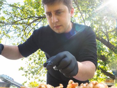 Siyah eldivenli yemek hazırlamak için doğadaki adam. Güneş, yeşil doğa.