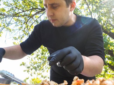 Siyah eldivenli yemek hazırlamak için doğadaki adam. Güneş, yeşil doğa.