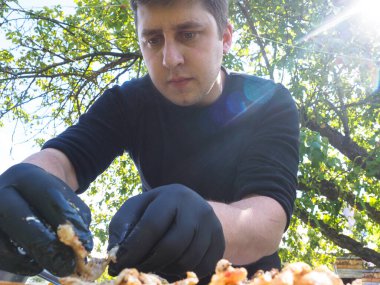 Siyah eldivenli yemek hazırlamak için doğadaki adam. Güneş, yeşil doğa.