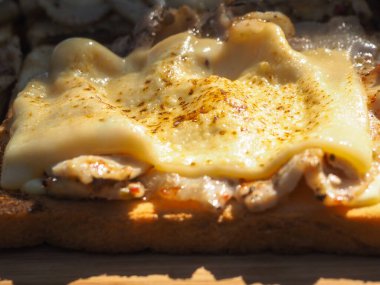 Domuz pastırmalı ve peynirli sandviç yapıyorum. Eldivenli eller sandviçleri toplar.