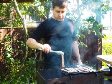 Bir adam ateşte et pişirir. Izgarada kızarmış pastırma. Doğada yemek yapmak.