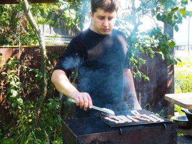 Bir adam ateşte et pişirir. Izgarada kızarmış pastırma. Doğada yemek yapmak.