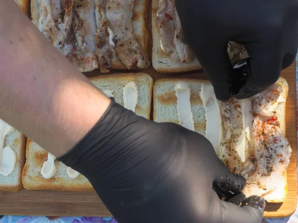 Pastırmalı sandviç yapıyorum. Eldivenli eller sandviçleri toplar.