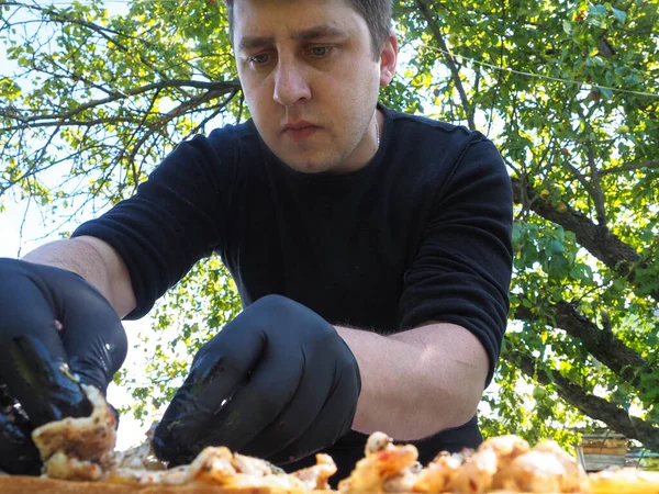the man on the nature to prepare food in black gloves. sun, green nature.